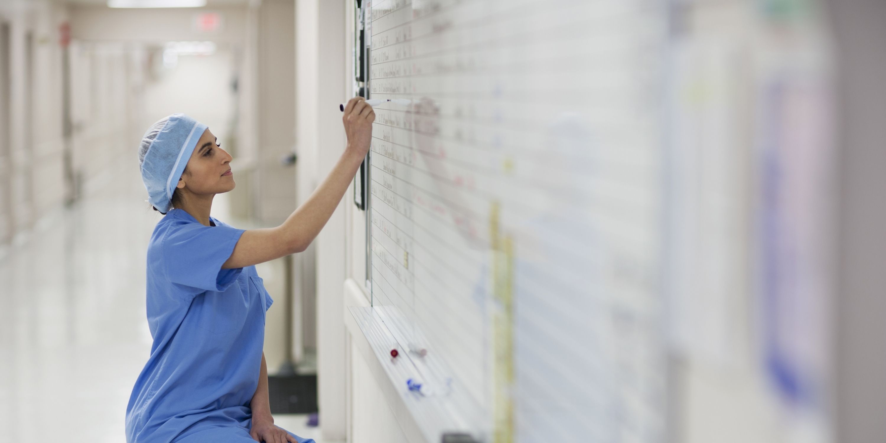 A nurse in scrubs writes notes on a whiteboard, focused on conveying important information to colleagues.