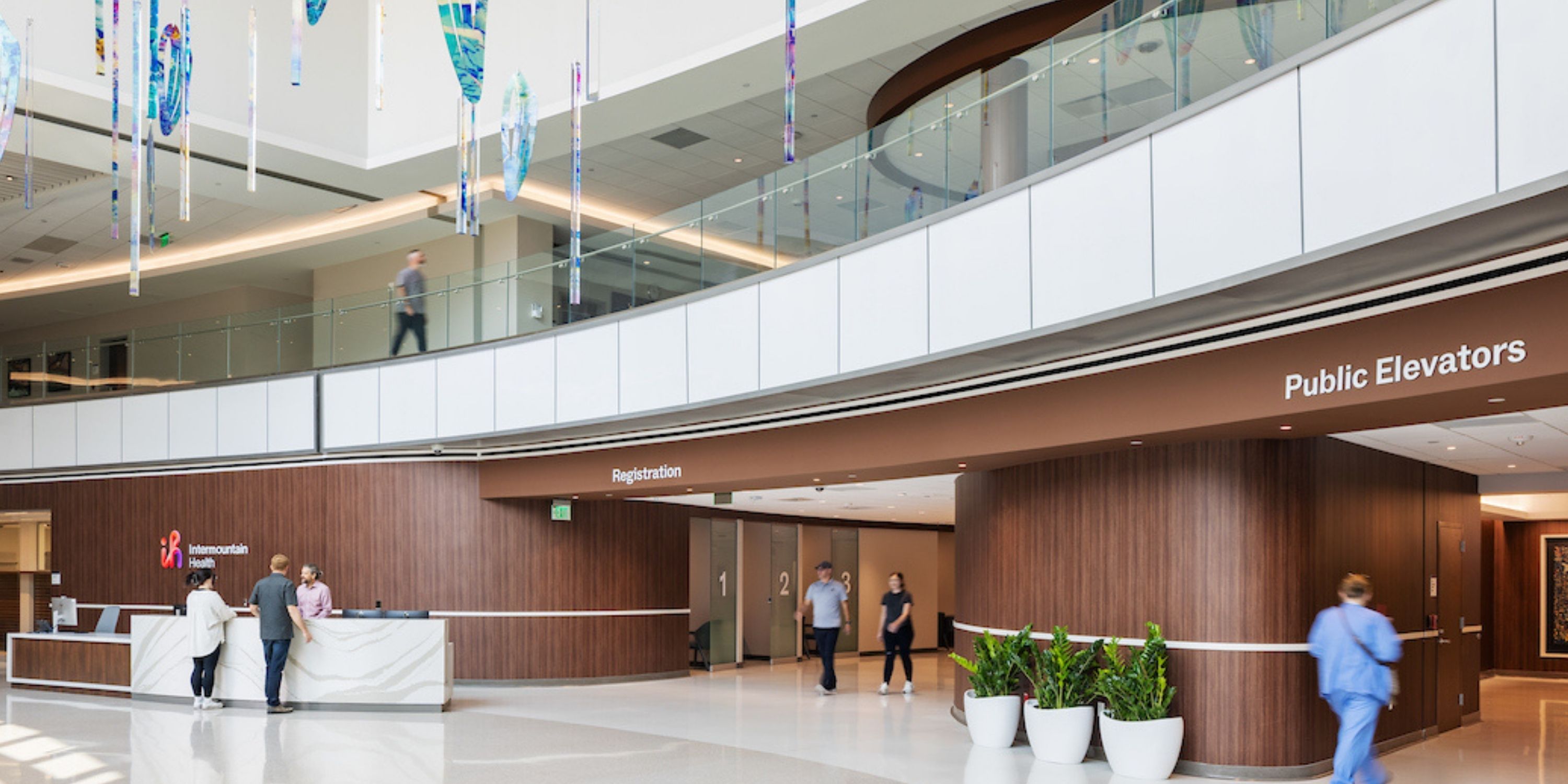 Hospital lobby scene featuring individuals walking, sitting, and interacting near reception and waiting areas.