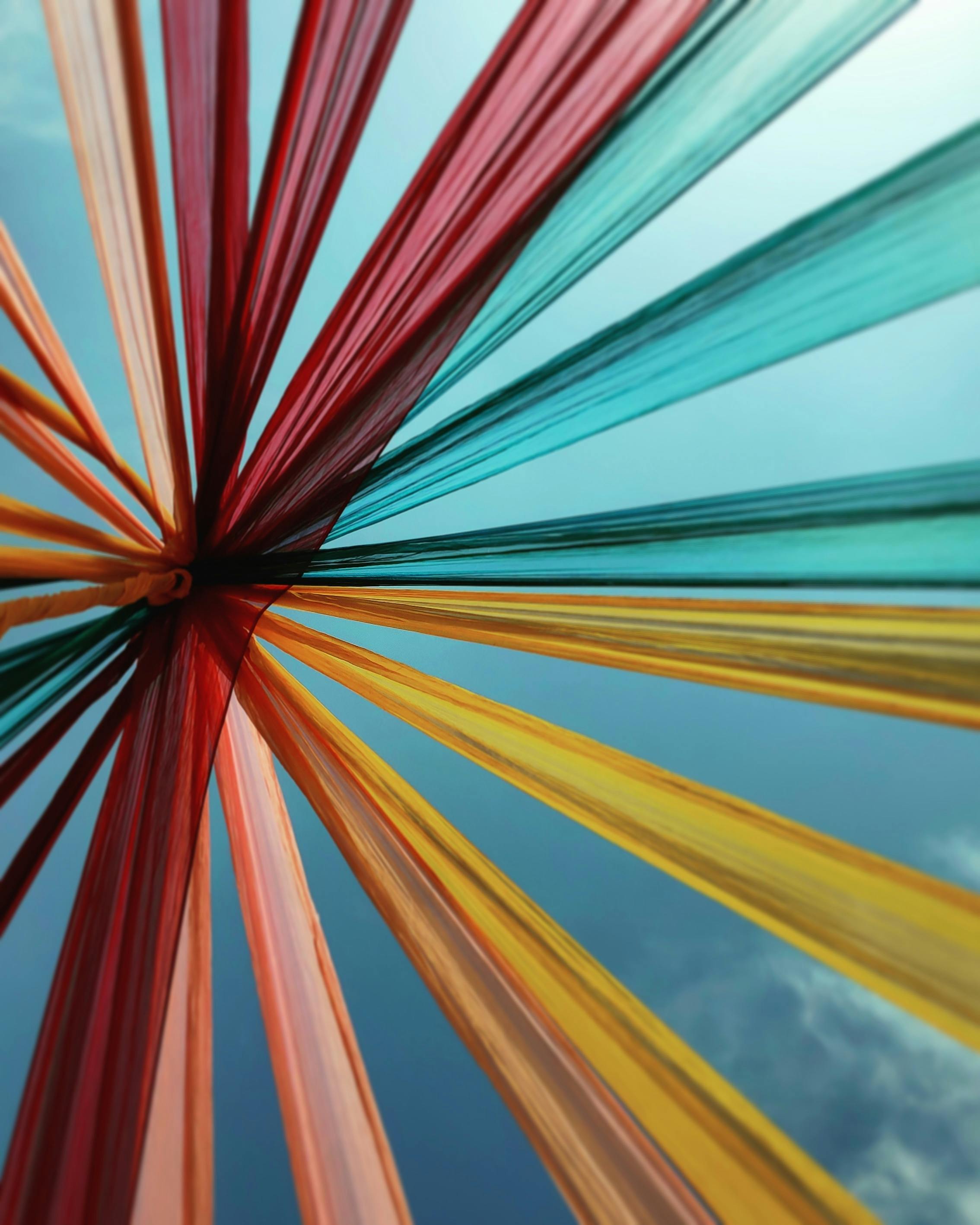 Colorful fabric strips radiate from a central point against a clear blue sky. The vibrant reds, oranges, yellows, and greens create a dynamic, festive atmosphere.