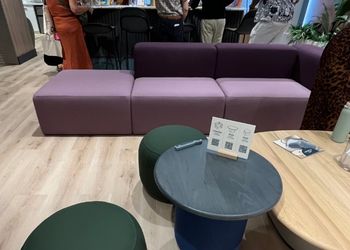 Large purple couch, green fabric stools, and a small black circle table.