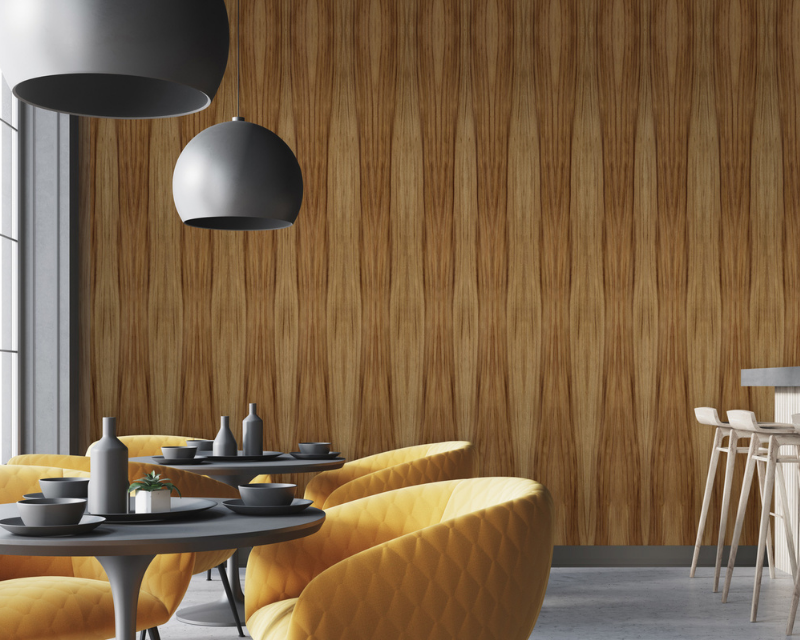 Modern cafe interior with yellow, quilted lounge chairs and dark gray tables on concrete flooring. A wood-patterned wall adds warmth, with large gray dome lights overhead.