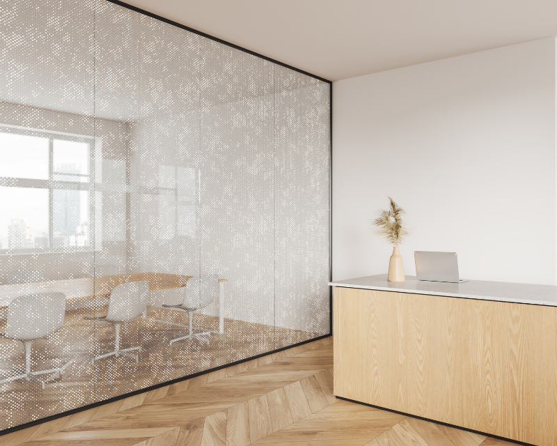 A modern office space with a patterned glass wall, wooden desk, laptop, and a minimalist vase with dried plants. Bright, serene, and clean ambiance.