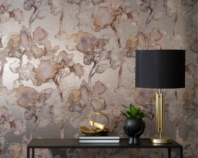 Artistic wallpaper with abstract trees in earthy tones covers a wall behind a sleek black table. A gold lamp, potted plant, and decorative gold object sit on the table, creating an elegant, serene atmosphere.