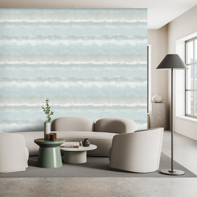 Modern living room with light gray couches and a green circular coffee table. The wall features a pastel blue and white striped pattern. Large window adds brightness.