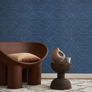 Modern interior with a dark brown chair, a light brown pillow, and a wood table with a sculptural vase. The blue geometric wallpaper adds a stylish touch.
