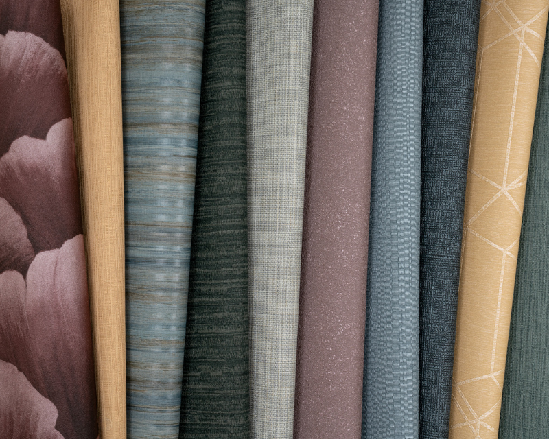 A collection of nine vertical fabric rolls in various colors. Patterns range from florals and textures to geometric designs, conveying a cozy, elegant feel.