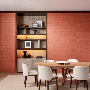 Modern dining room with a round wooden table, six white fabric chairs, red textured walls, and a lit bookshelf with decor items, creating a warm ambiance.