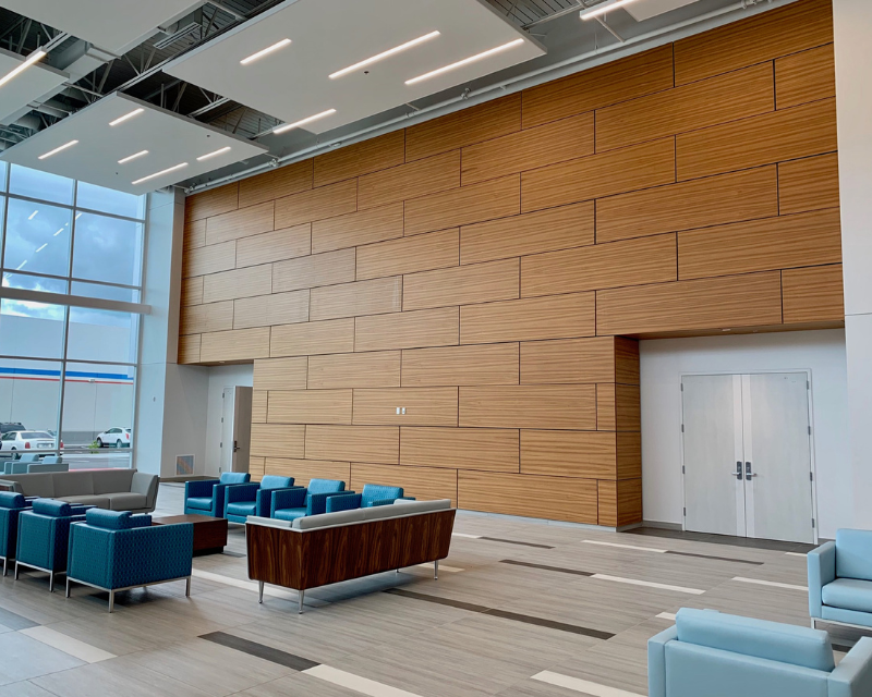 Modern lobby with a high wooden panel wall, blue seating, and large windows. The bright space is airy and welcoming with sleek lines and natural light.