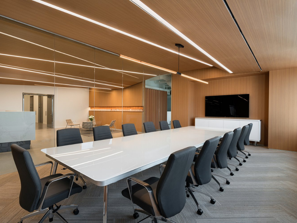 HERITAGE-WOOD-II-(2).png Modern conference room with a long white table, surrounded by black chairs on a gray carpet. Wood covered walls, wood covered ceiling, and a mounted TV create a sleek atmosphere.