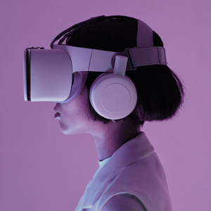 A person wearing a VR headset and large headphones, viewed from the side against a purple background. The tone is futuristic and immersive.
