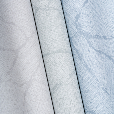 Three overlapping fabric rolls, each featuring a delicate marble-like pattern. The colors transition from light grey to pale blue, creating a calming effect.